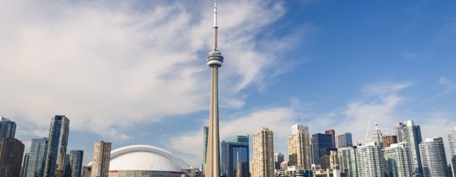 Toronto skyline featuring the cn tower and rogers centre against a backdrop of blue sky and fluffy clouds, viewed from the water with boats visible.