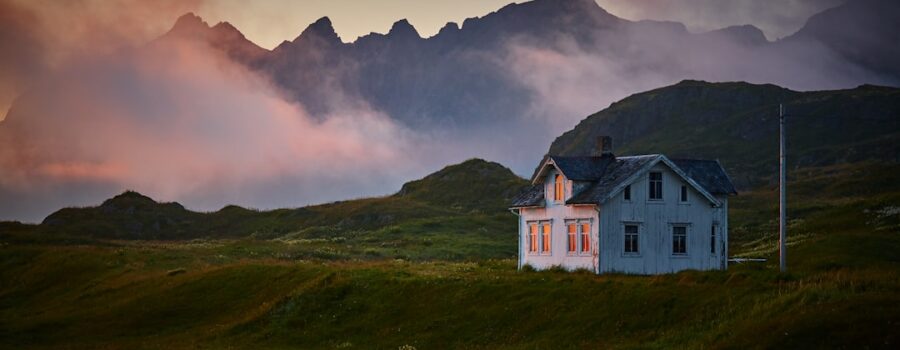 White house on a grassy field with mountains and mist in the background during sunset.