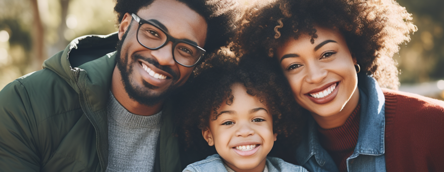 A family of three smiles while seated outdoors on a sunny day with trees in the background, perhaps celebrating their journey together under an Open Work Permit.