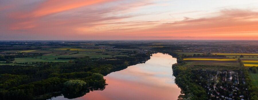 Aerial view of a river reflecting vibrant pink and orange sunset sky, surrounded by green fields and a small town.